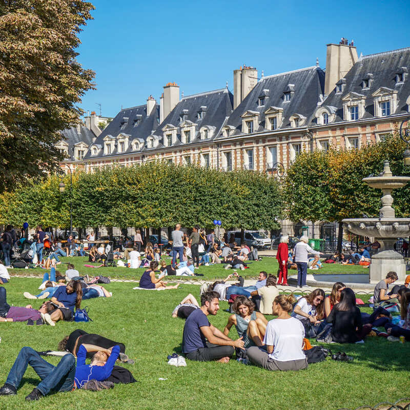 A Crowd Of Tourists And Locals Enjoying A Sunny Day In Place des Voges In Paris, France, Europe