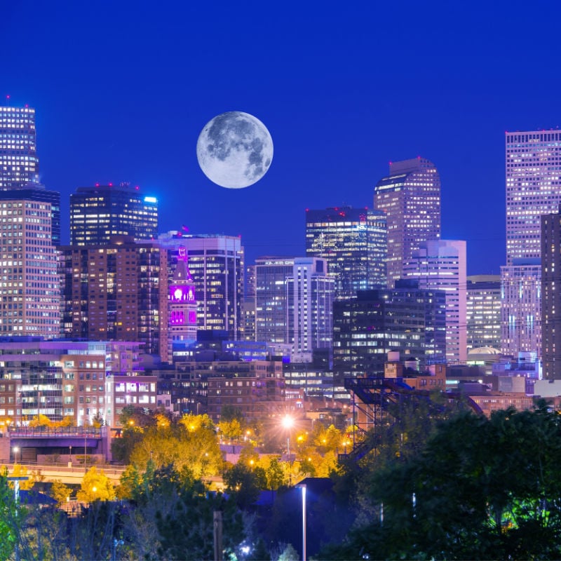 denver city skyline at night with full moon hanging above buildings