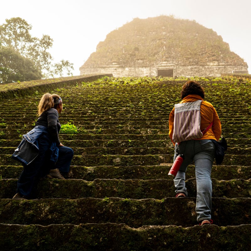 two travelers ascend the steps at tikal maya ruin in guatemala